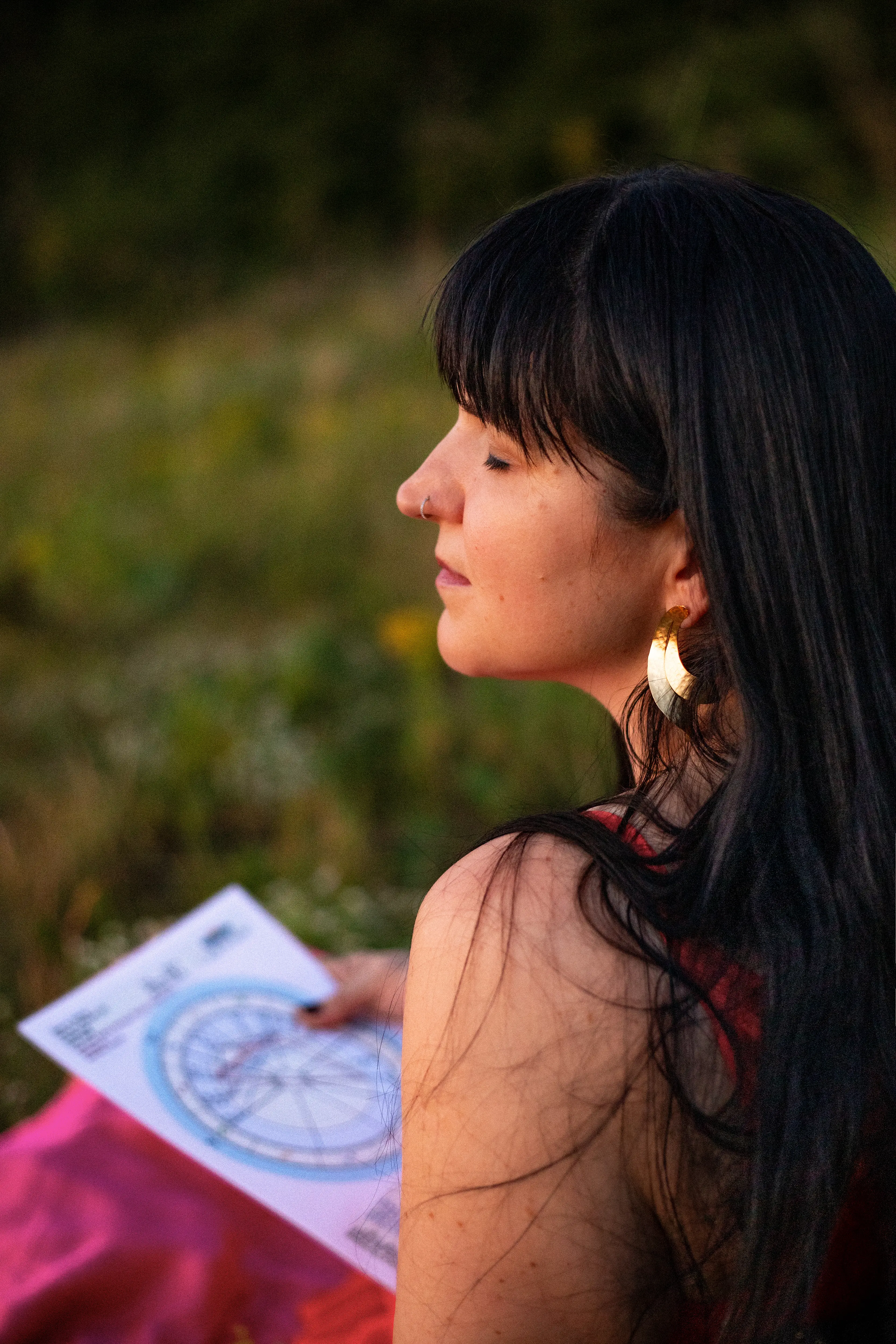 Adrienne sentada en un campo iluminado por el sol con su carta natal impresa y una vela encendida