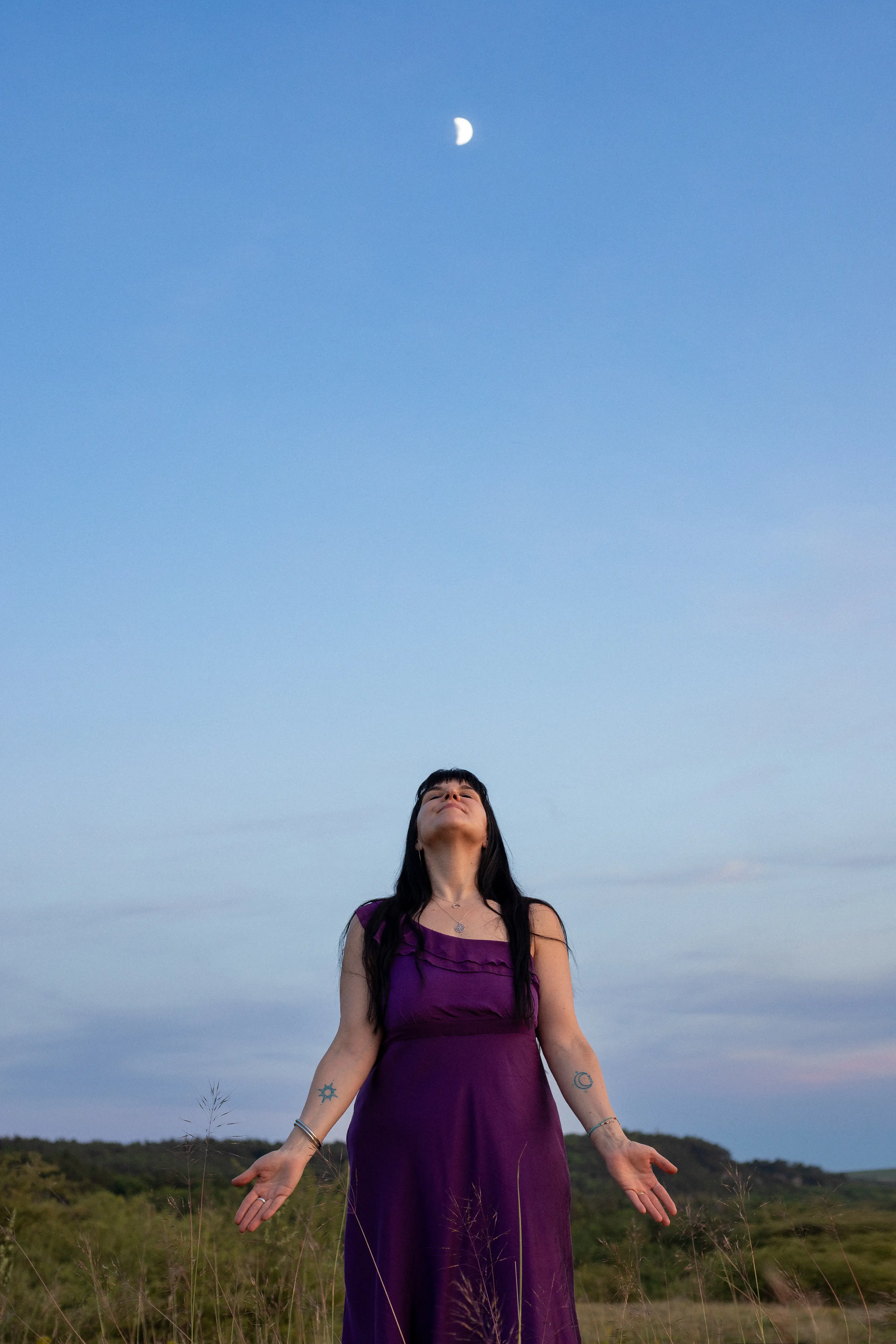 Adrienne with arms outstretched holding a flowing red shawl beside the water at golden hour